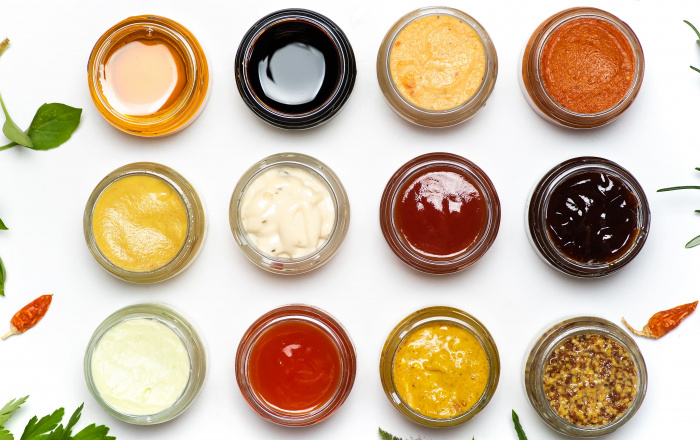 Jars of various condiments on white background and bordered with herbs