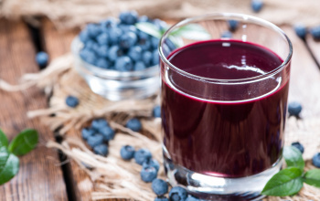 Glass of blueberry juice with blueberries in the background